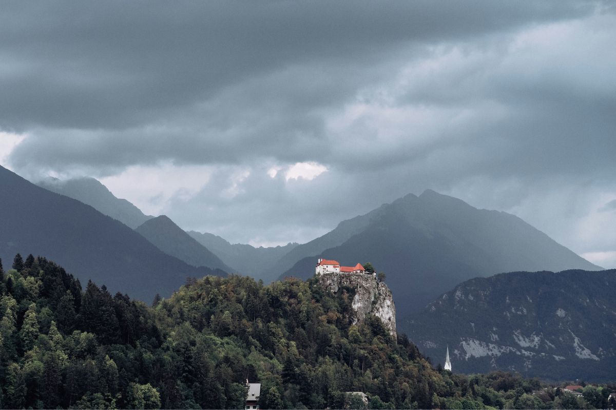 Srednjovjekovni Bledski dvorac na vrhu strme litice iznad jezera u Sloveniji pod oblačnim nebom.
