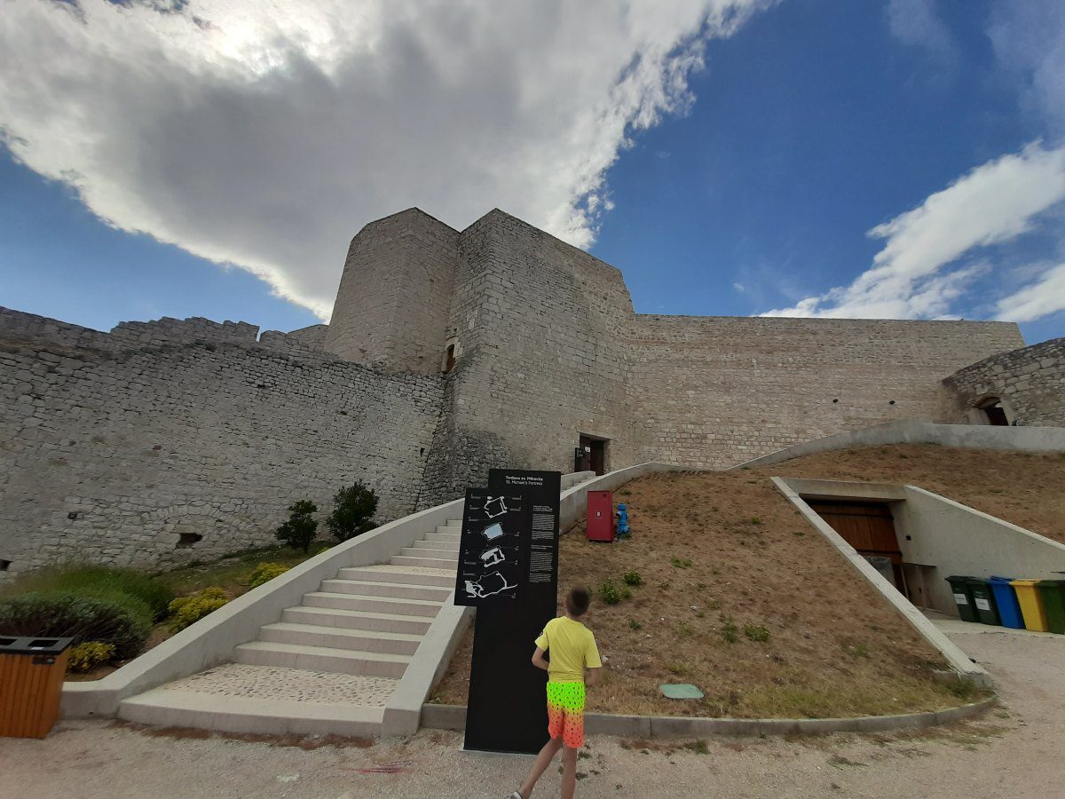 Visoki kameni zidovi povijesne Tvrđave sveti Mihovil u Šibeniku pod plavim nebom i bijelim oblacima.